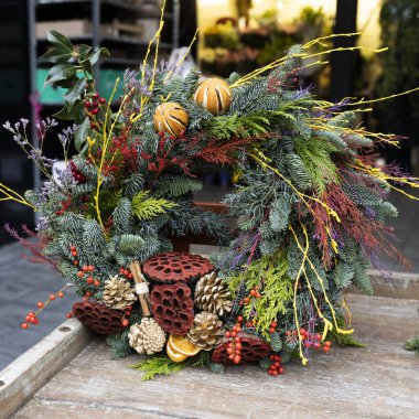 Noel çelengi kuru mandalinalar, nilüferler, otlar, yeşil ve turuncu renkli meyveler ile süslenmiş olarak markette satılmaktadır.