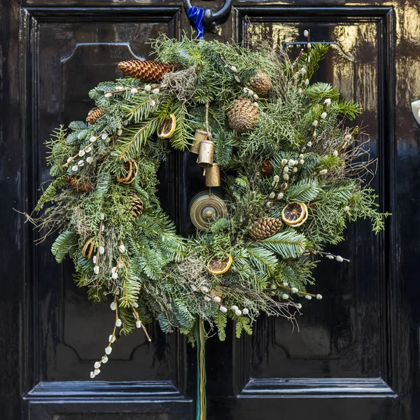 Christmas wreath made of sprigs of fir, juniper, willow, with fir cones, dried orange circles, bells and moss on a black London door
