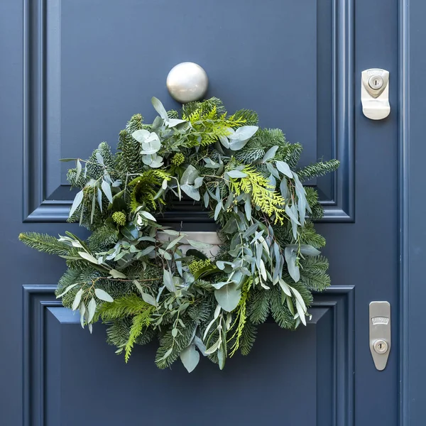 A modest Christmas wreath made of sprigs of fir, thuja, eucalyptus on a dark blue door in London. Square frame.