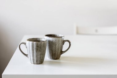 Beyaz masada iki porselen gri bardak var..