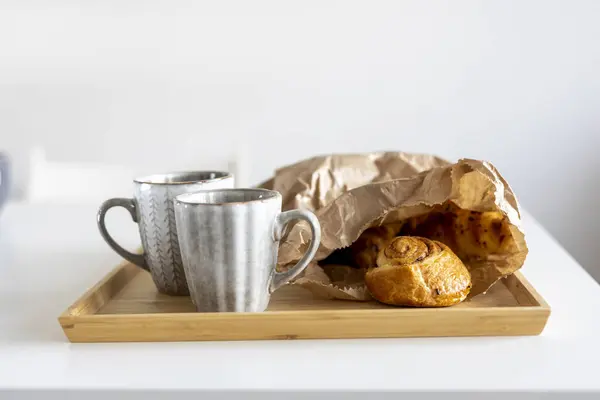 Croissants with chocolate chips on a craft paper on the table, a gray cup with a white heart with tea. Place for text