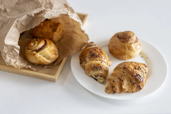 Fresh pastries - croissants with chocolate chips, poppy seed buns on a white sheet of paper on the table. Place for text