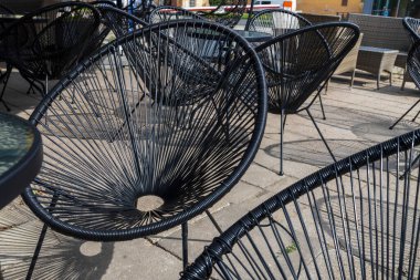 Güneşli havada gölge oluşturan çubuklardan yapılmış yarı dairesel demir koltuklar.