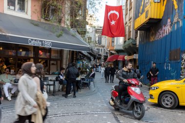 Istanbul, Turkey - April 10, 2024, People sit on the veranda of a cafe in the Balata district during Ramadan. A man rides a motorcycle. clipart