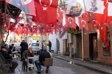 İstanbul, Türkiye - 10 Nisan 2024, Erkekler bir sokak kafesinde oturur, çay içer, konuşur ve sigara içerler. Yolun üzerinde Türk bayrakları ve liderlerin portreleri asılı.