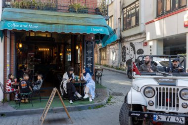 İstanbul, Türkiye - 10 Nisan 2024, Ramazan boyunca Balata ilçesindeki bir kafenin verandasında insanlar oturuyor. Açık bir cipin içindeki adamlar yoldan geçiyorlar..