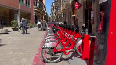 BARCELONA, İspanya - 25 Nisan 2024: Kiralık kırmızı motorlar grubu. Bisikletler şehir merkezindeki turistlerin yanında Katalan Müzik Sarayı 'nın yanında 