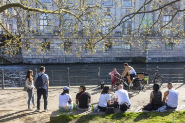 Berlin, Almanya - 02 Nisan 2024, Halk müze adasının yakınındaki sette oturur, kanal boyunca bir tekne hareket eder - Berlin 'de ilkbahar. Genç kadınlar ve genç erkekler müzik dinlerler.