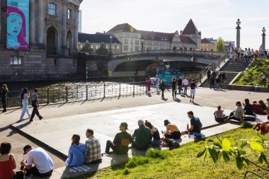 Berlin, Almanya - 02 Nisan 2024, İnsanlar setin üzerinde oturuyorlar. Berlin 'de ilkbahar. Neşeli insanlarla dolu bir eğlence gemisi kanal boyunca yol alıyor..