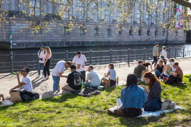 Berlin, Almanya - 02 Nisan 2024, Halk müze adasının yakınındaki sette oturur, kanal boyunca bir tekne hareket eder - Berlin 'de ilkbahar. Genç kadınlar ve genç erkekler birlikte vakit geçiriyorlar.