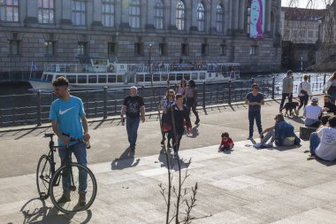 Berlin, Almanya - 02 Nisan 2024, İnsanlar setin üzerinde oturuyorlar. Berlin 'de ilkbahar. Neşeli insanlarla dolu bir eğlence gemisi kanal boyunca yol alıyor..