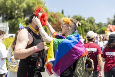 Hayfa, İsrail 21 Haziran 2024, gökkuşağı bayrağına sarılmış bir adam arkadaşının sahte tüylerden yapılmış kırmızı kedi maskesi takmasına yardım ediyor..