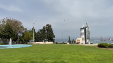 Hayfa, İsrail - 20 Mayıs 2024. Savunma Bakanlığı 'nın yelken, deniz ve liman şeklindeki manzarasının yanı sıra belediye binasının yakınında fıskiyeler ve incir ağaçları olan bir park..