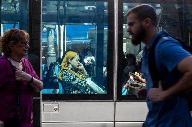 Kudüs, İsrail - 30 Eylül 2024. Sarı başörtülü Ortodoks bir kadın otobüse biniyor ve telefonla konuşuyor. Rastgele yoldan geçenlerle pencereden bak.