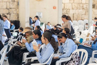 Jerusalem, Israel - September 30, 2024, Twelve-year-old girls in identical school uniforms sit on chairs, holding the Tanakh in their hands and praying at the Western Wall on the eve of Rosh Hashanah. clipart