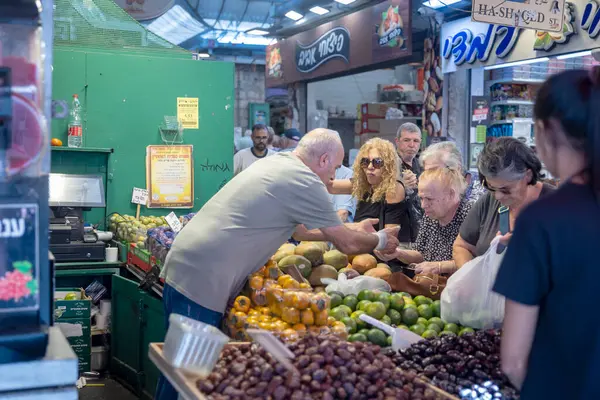 Kudüs, İsrail - 1 Ekim 2024. Kippah 'taki bir adam Mahane Yehuda pazarındaki ziyaretçilere sebze satıyor..