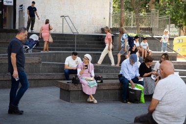 Kudüs, İsrail - 1 Ekim 2024, insanlar şehir merkezindeki taş basamaklarda ve banklarda dinleniyor. Hem Ortodoks hem de laik, kadınlar ve erkekler.