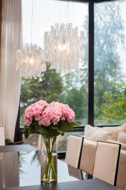 Hollanda Pembe Ortancası, pencerenin karşısındaki dekoratif avizenin altında cam bir vazoda duran uzun bir buket..
