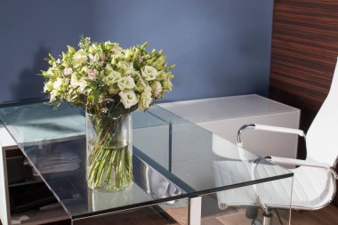 Bir buket Macropidia, lisianthus ve okaliptüs çalışma odasındaki mavi bir duvarın karşısında bir masanın üzerinde duruyor. Minimalist kompozisyon.