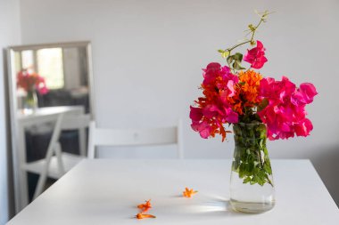 Turuncu çiçekli ve ahududu çiçekli bir buket kamp dalı beyaz bir masadaki aynaya yansıyor. Metin için boşluk.