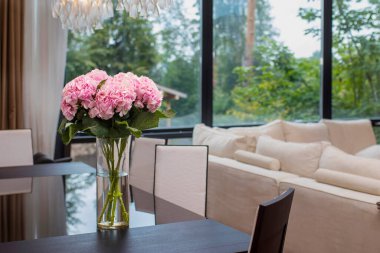 Ofisteki bir müzakere masasında silindirik cam vazoda sergilenen pembe ortanca buketi, beyaz sandalyeler ve arka planda beyaz desenli bir duvar ile tamamlanmış..