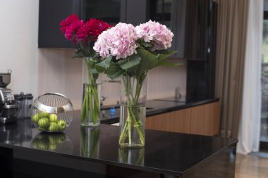  Bir buket pembe Hollanda ortancaları ve bir buket kırmızı yıldız çiçeği ile modern bir mutfak masasında yeşil elmalarla dolu bir vazo..