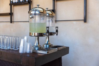 Bir sürahi içinde limonata ve bardaki masada plastik bardaklar..