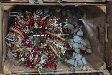 Markette satılık bir Noel çelengi, tahta bir kutuda. Çelenk kozalaklı dallardan, yapay okaliptüs filizlerinden ve kutsal dutlardan yapılmıştır..