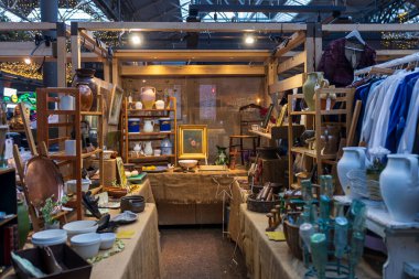 Londra, İngiltere - 22 Kasım 2024. Spitalfields Market 'teki bit pazarı. Masa lambaları, zemin lambaları, sürahiler, raflardaki ev eşyaları, vinil plaklar, satılık bej kumaşlara karşı.