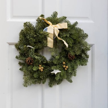 Yeşil köknar çelengi ve çam dalları gümüş ahşap yıldızlar, altın Noel topları ve büyük bir fiyonk beyaz bir İngiliz kapısını süslüyor..