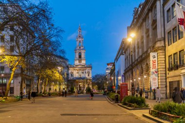 Londra, İngiltere - 1 Aralık 2024: St Mary le Strand Kilisesi, kırmızı bir retro telefon kulübesi ve alacakaranlıkta etrafında yayalar.