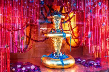 London, UK - December 2, 2024: A Christmas window display at Selfridges. A golden pedestal featuring perfumes and colognes against a backdrop of red tinsel and garlands. clipart