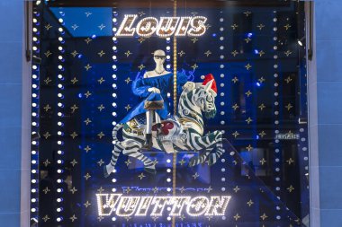 Londra, İngiltere - 2 Aralık 2024: Louis Vuitton 'da Noel vitrini. Fuar teması. Mavi elbiseli bir manken, kolunda altın deri bir çanta, atlıkarınca zebrası sürüyor, kırmızı bir Noel şapkası takıyor..