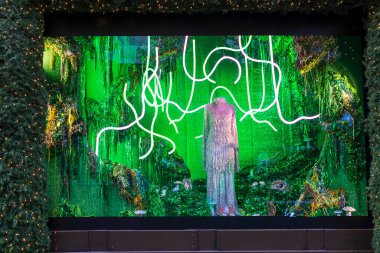 Londra, İngiltere - 2 Aralık 2024: Selfridges 'de Noel vitrini. Uzun kürklü bir elbise, ayakkabılar ve parlak yeşil asit arka planına karşı neon tüpleri..