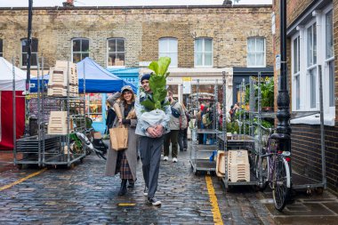 Londra, İngiltere - 2 Aralık 2024: Gülümseyen genç bir adam ve kadın saksı bitkisi satın aldılar ve onu eve taşıyorlar.