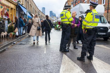Londra, İngiltere - 2 Aralık 2024: Columbia Çiçek Pazarı. Kadın bir çiçekçi polis memurlarıyla sohbet ediyor..
