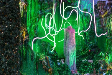 Londra, İngiltere - 2 Aralık 2024: Selfridges 'de Noel vitrini. Uzun kürklü bir elbise, ayakkabılar ve parlak yeşil asit arka planına karşı neon tüpleri..