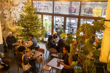 Londra, İngiltere, 1 Aralık 2024 İnsanlar Brick Lane 'deki Hipster Kafe 1001' de oturuyor. Kafe bir Noel ağacıyla süslenmiş..