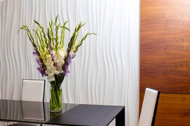 Cam bir masadaki cam vazoda beyaz desenli bir duvarın karşısında duran bir buket beyaz ve mor leylak çiçekleri..