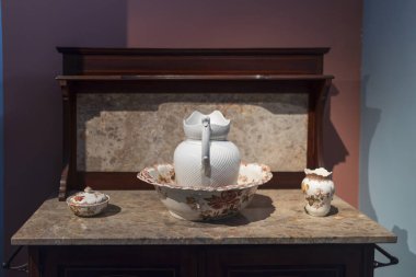 Büyük bir kasede kuğu şeklinde saplı beyaz bir sürahi. Bir vazo ve bir şeker kasesi eski ahşap bir masanın üzerinde..