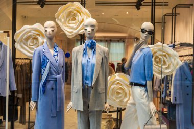 Vitrinde mavi bluzlar olan gri ceketli ve pantolonlu soyut mankenler.