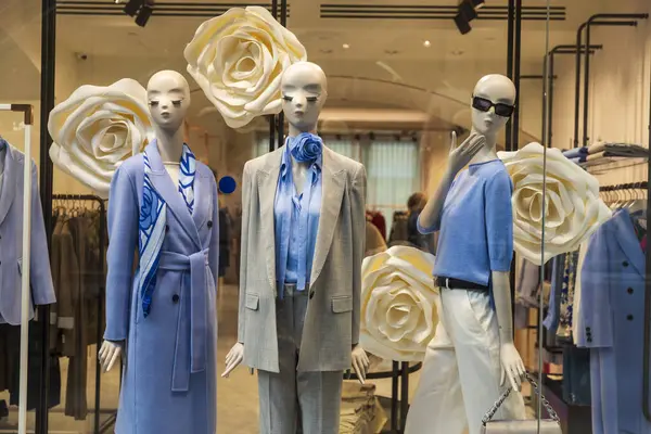 Vitrinde mavi bluzlar olan gri ceketli ve pantolonlu soyut mankenler.