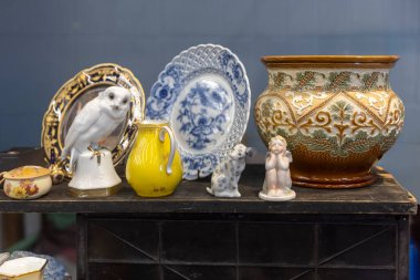 Londra, İngiltere - 2 Aralık 2024. Covent Garden 'daki klasik Jubilee Pazarı. Sarı bir sürahi, beyaz bir baykuş heykeli, porselen bir melek, eski bir Çin vazosu, ve bit pazarında satılık bir masada bir peri köpeği..