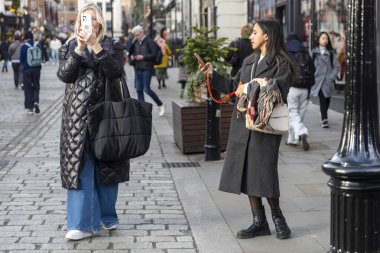 Londra, İngiltere - 2 Aralık 2024. Covent Garden 'daki kalabalıkta iki kadın cep telefonuyla fotoğraf çekiyor..