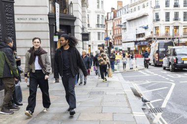 Londra, İngiltere - 4 Aralık 2025, Regent Caddesi 'nde yürüyüş yapan iki şık giyimli genç adam. Sokak tarzı.