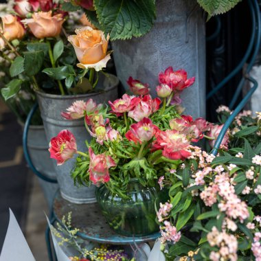 Kırmızı şakayık ve düğün çiçekleri, yuvarlak cam bir vazoda metal bir sandalyede, iç dekorasyon için bir buket turuncu gülle ve düğün, tarih ve cenaze törenleriyle çevrili.