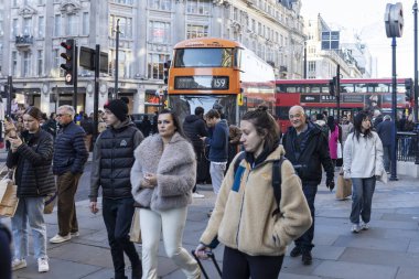Londra, İngiltere. 3 Aralık 2024. Kalabalık, yoğun saatlerde Oxford Caddesi 'nde yürüyor. Farklı ırktan insanlar. Sahte kürklü bir kadın kalabalığın ortasında dikiliyor. Kırmızı çift katlı bir otobüs dönüyor..
