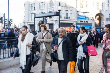 Londra, İngiltere. 3 Aralık 2024. Kalabalık Oxford Caddesi boyunca yoğun saatlerde yürüyor. Farklı ırktan insanlar. Siyah bir adam, kızıl saçlı genç bir adam kulaklıkla müzik dinliyor..