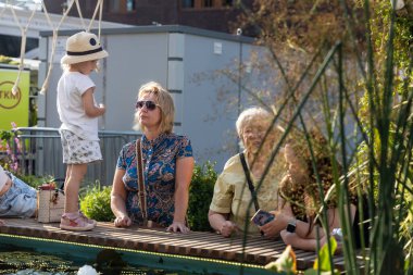 Moskova, Rusya - 25 Ağustos 2024, güneş gözlüklü bir büyükanne bariyerin önünde duran üç yaşındaki torununa sert bir şekilde bakıyor..