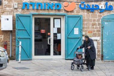 Acre, İsrail 23 Ocak 2025, yaşlı, ciddi ve yorgun bir Arap kadın tesettüre bürünmüş bir yürüyüşçüyle eski şehrin sokaklarında yürüyor..